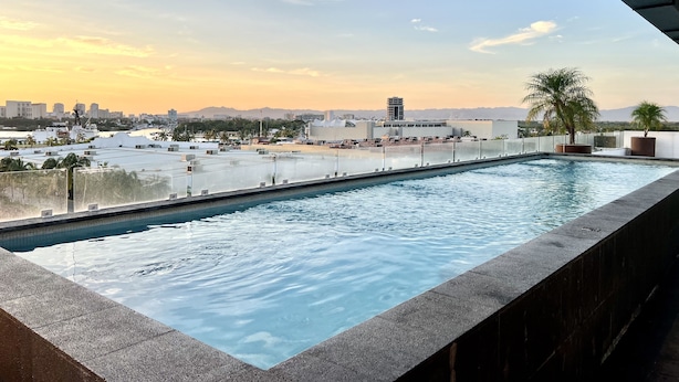 Une piscine sur le toit offrant une vue panoramique sur la ville, avec ses bâtiments et ses palmiers.