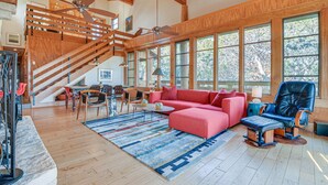 A spacious living area with a wooden staircase, large windows, a red sectional sofa, a leather recliner, and a dining area with wooden furniture. - Lake Whitney Cabin w/ Hot Tub & Fire Pit! (Morgan)