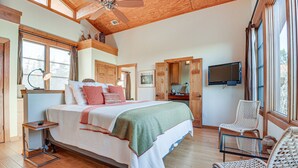 A spacious bedroom with a large bed, wooden ceiling, and a television mounted on the wall. - Lake Whitney Cabin w/ Hot Tub & Fire Pit! (Morgan)