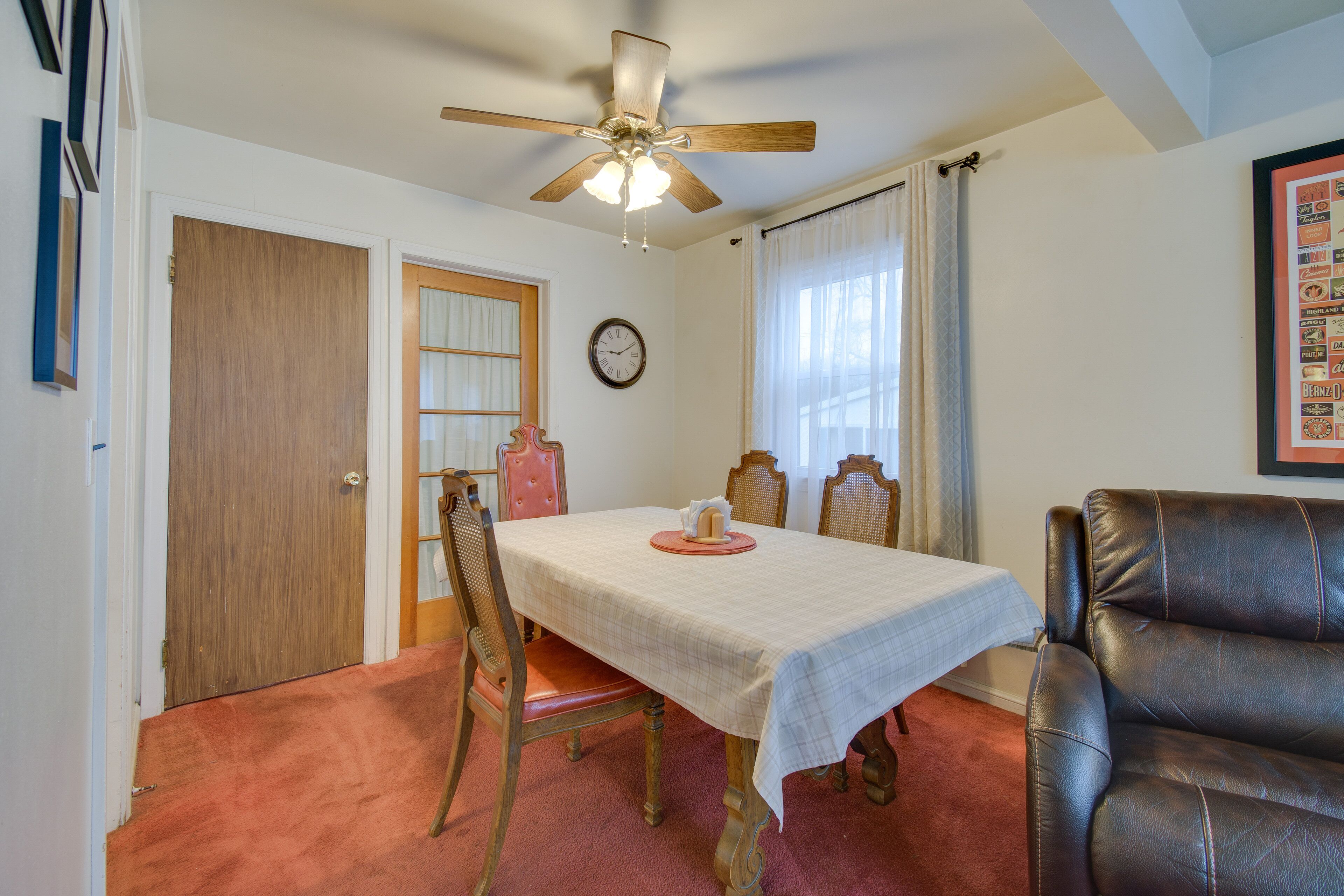 Un espace repas comprenant une table, des chaises, un ventilateur de plafond, une horloge et un menu encadré accroché au mur.