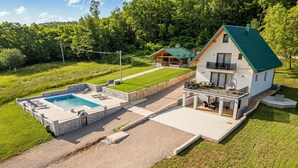 Et moderne hus med to etager, swimmingpool, udendørs møbler og en velplejet græsplæne.