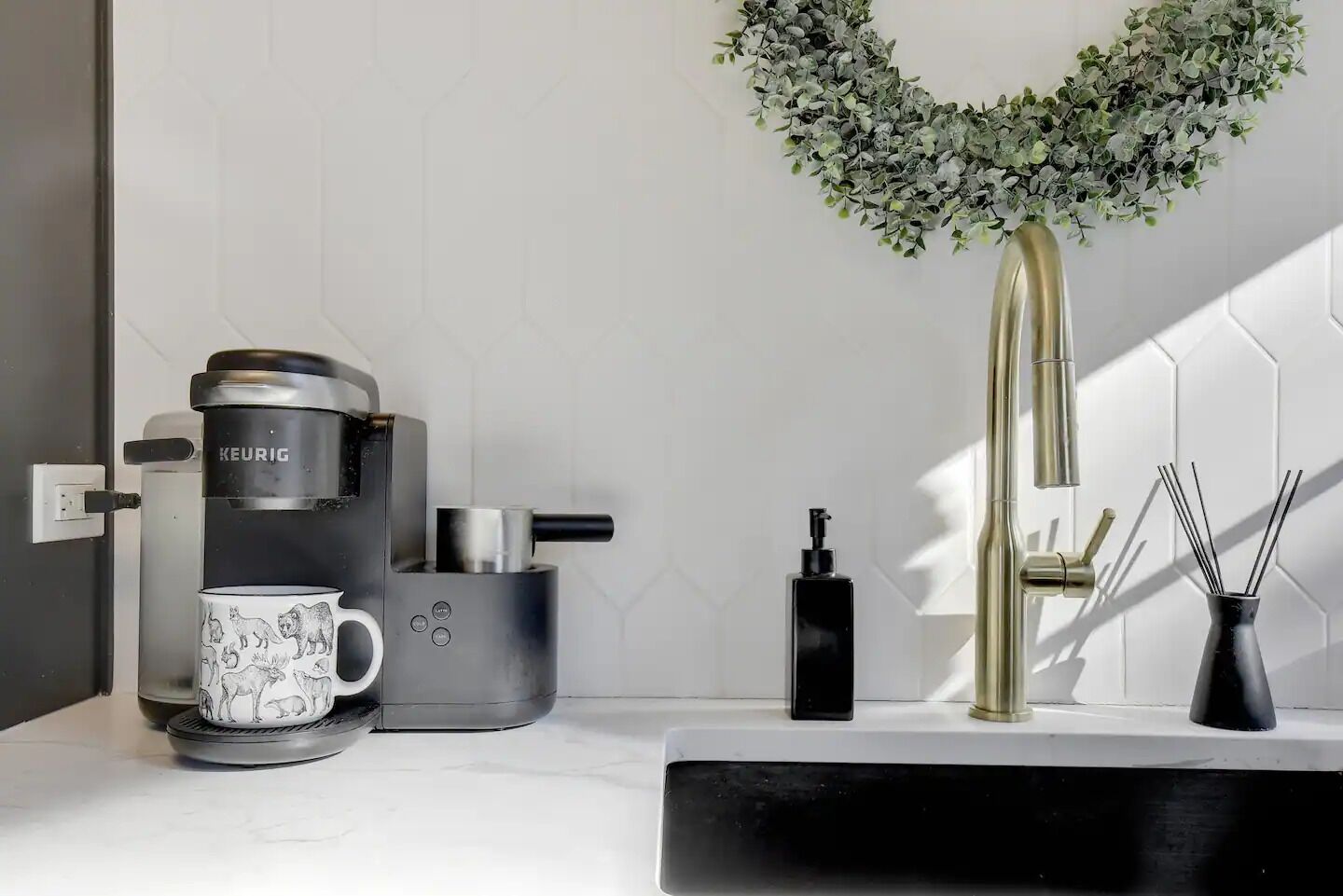 A modern kitchen with a coffee maker, a sink, a soap dispenser, and a decorative plant.