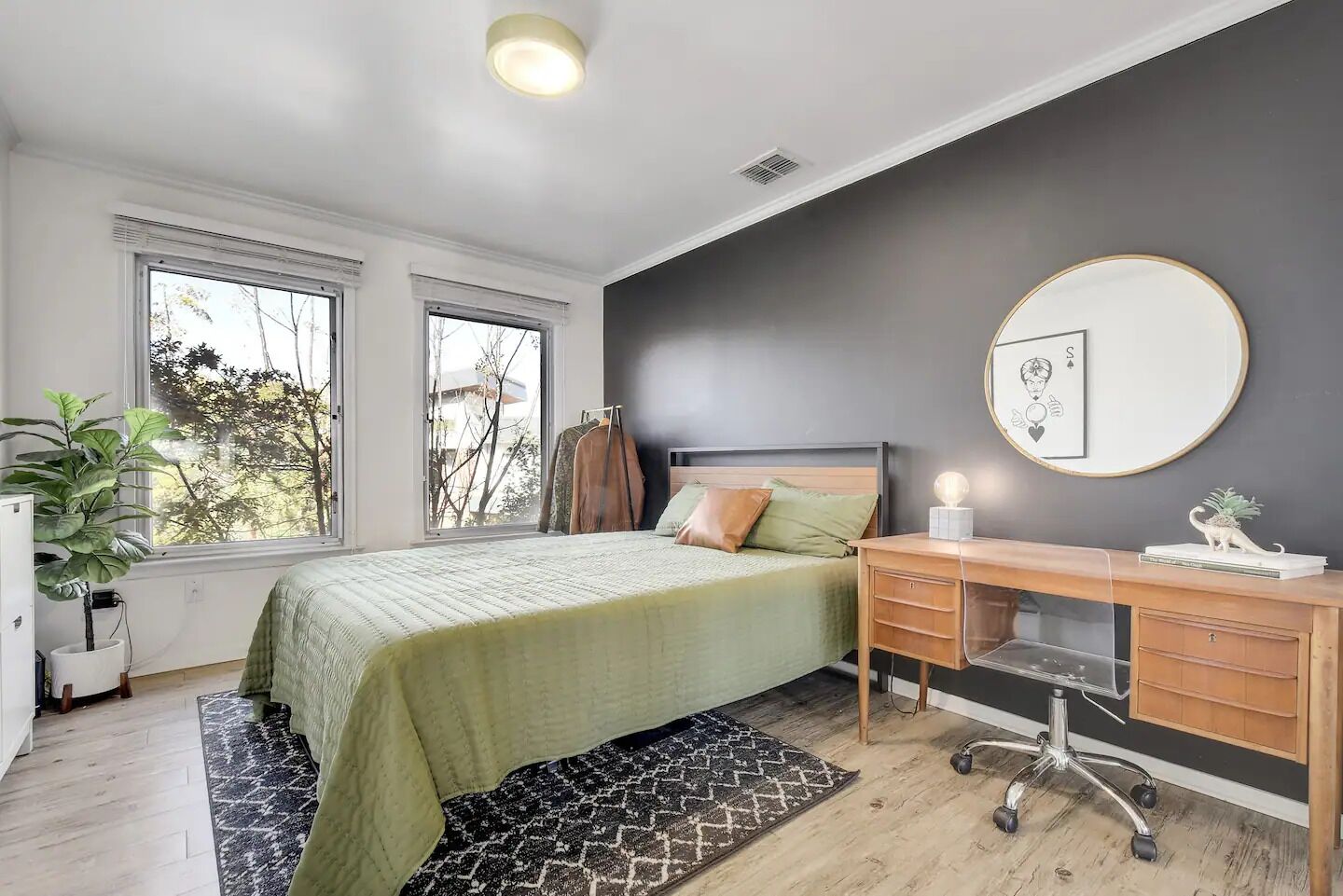 Une chambre à coucher avec un lit, un bureau, une chaise, une plante en pot et une fenêtre.
