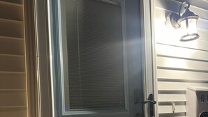 Una puerta corrediza de vidrio con marco blanco, una ventana pequeña y una barandilla blanca.