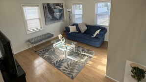 Una sala de estar con un sofá azul, una mesa de centro de vidrio y una alfombra estampada.