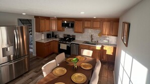 Una cocina moderna con armarios de madera, electrodomésticos de acero inoxidable y un comedor con una mesa de madera dispuesta para cuatro comensales.