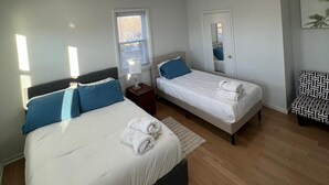Habitación de hotel con dos camas, una ventana, una puerta, un espejo y una lámpara en el techo.