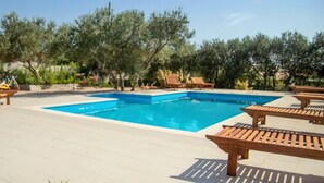 Ein rechteckiger Pool mit Fliesen umgeben, mit Holzliegen und Bäumen.