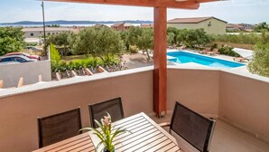 Ein Balkon mit Tisch und Stühlen, Blick auf einen Swimmingpool und umgebende Grünflächen.