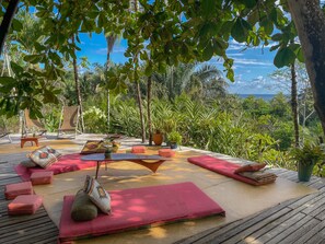A deck with outdoor seating, including chairs and cushions, surrounded by lush greenery and a view of the ocean. - Finca Exotica ecolodge (Puerto Jiménez)