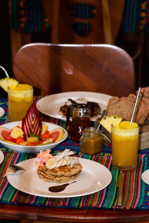 A breakfast setting with a plate of pancakes, a glass of orange juice, and a fruit bowl. - Finca Exotica ecolodge (Puerto Jiménez)