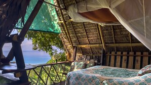 A room with a bed, a table, and a view of the ocean. - Finca Exotica ecolodge (Puerto Jiménez)