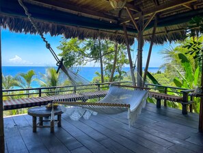 A hammock under a thatched roof, a wooden table with a bottle, and a view of the ocean. - Finca Exotica ecolodge (Puerto Jiménez)