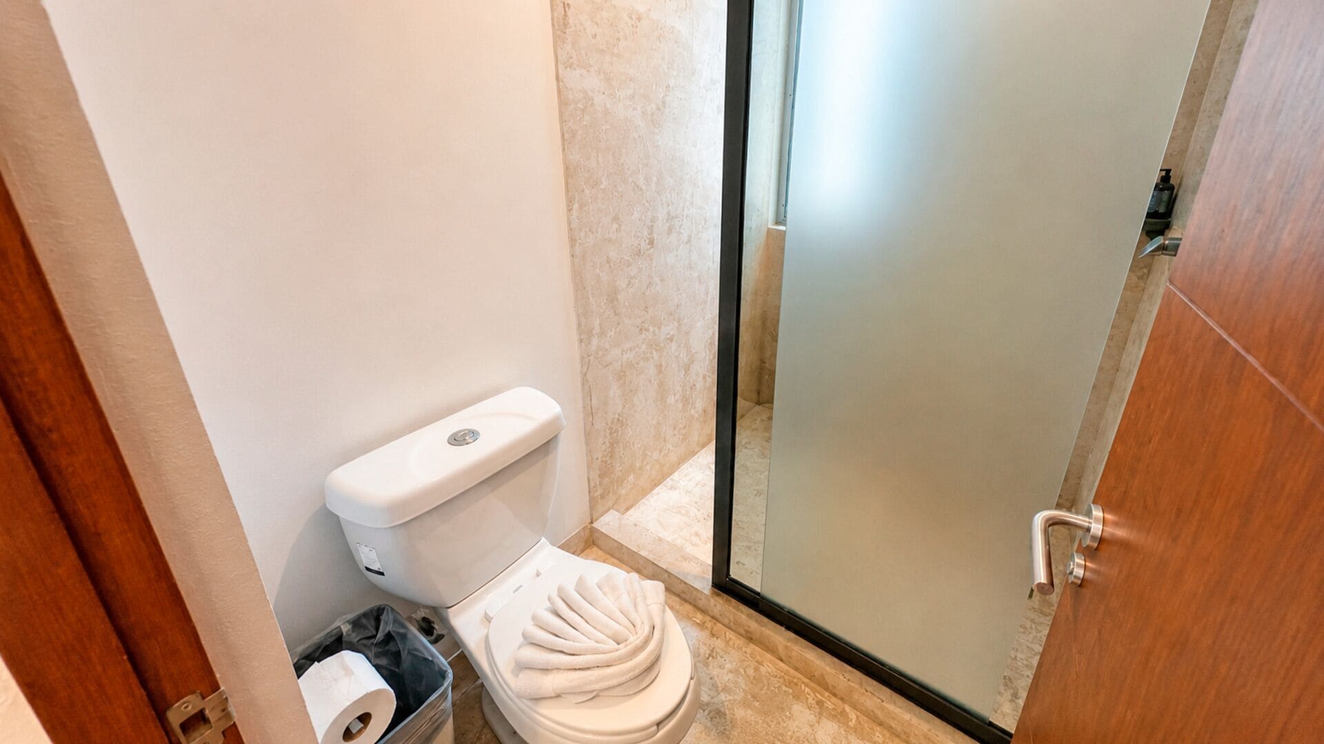 Une petite salle de bain comprenant des toilettes, une poubelle et une porte de douche en verre.
