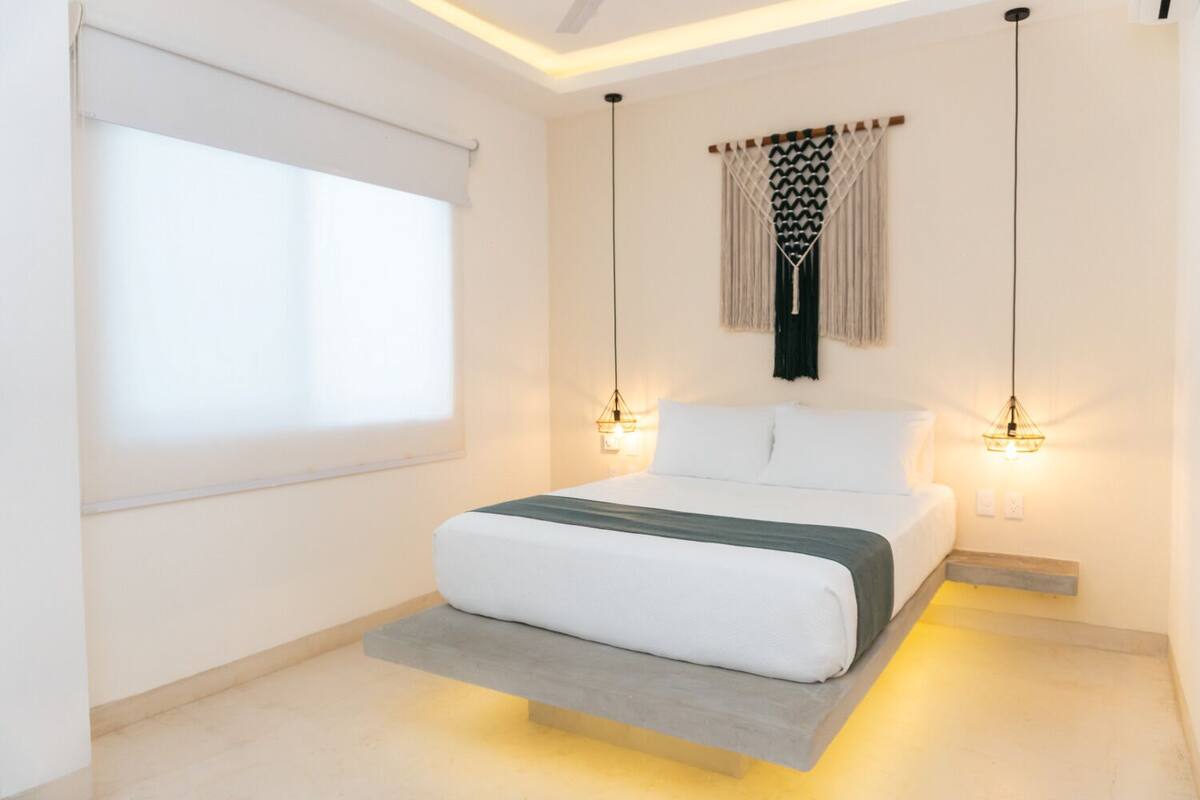 Un dormitorio moderno con una cama ubicada en una plataforma, un ventanal con persianas y dos lámparas colgantes.
