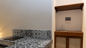 A room with a patterned bed, a wooden cabinet with a sink, and a small framed picture on the wall. - Kanté Hotel - Downtown Tulum (Tulum)