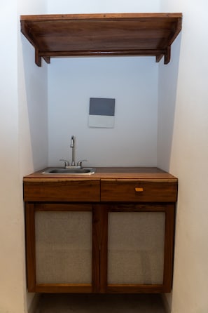 Uma cozinha compacta com bancada de madeira, uma pia e dois armários com portas de tecido.