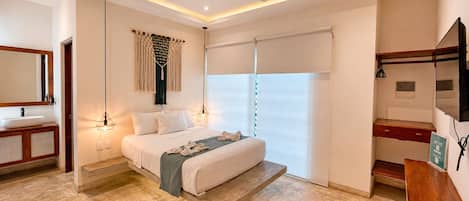 A bedroom with a bed, bedside lamps, a ceiling fan, a large window with blinds, a wooden dresser, and a mirror.
