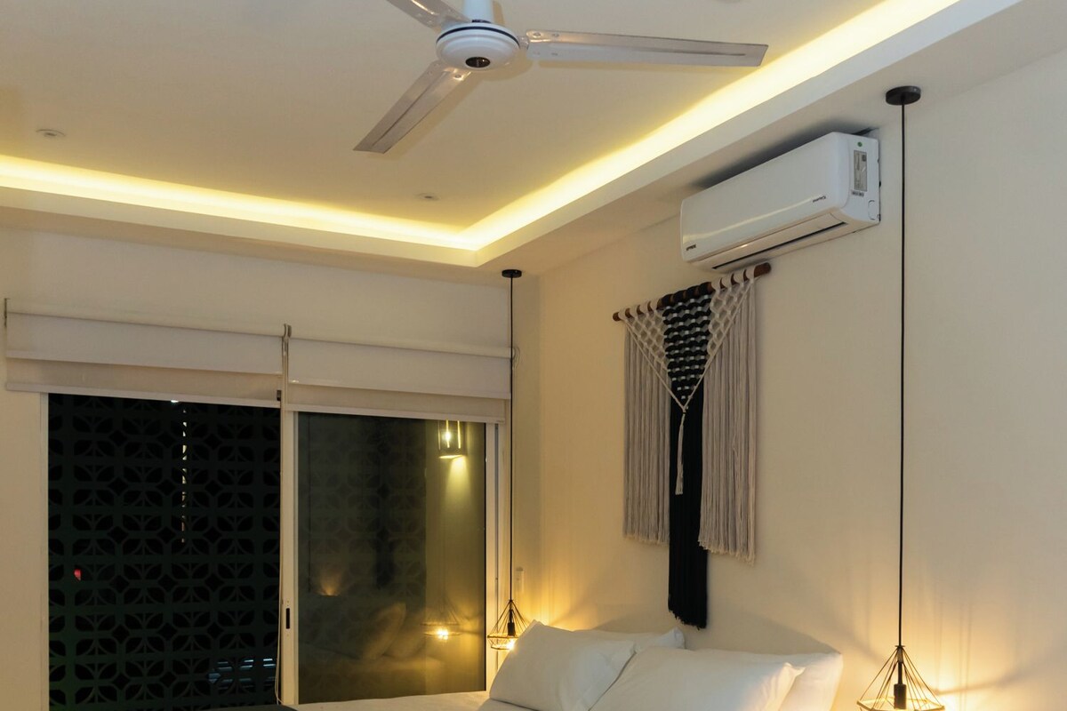 Une chambre moderne avec un lit suspendu au plafond, un appareil de climatisation, un ventilateur de plafond et une décoration murale en macramé.