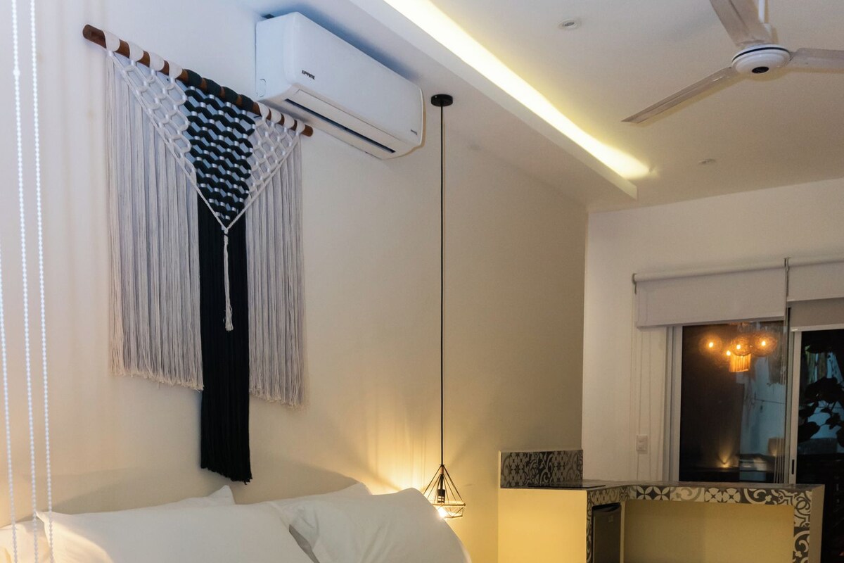 Un dormitorio moderno con una cama grande, un ventilador de techo, un equipo de aire acondicionado y una mesita de noche con lámpara.