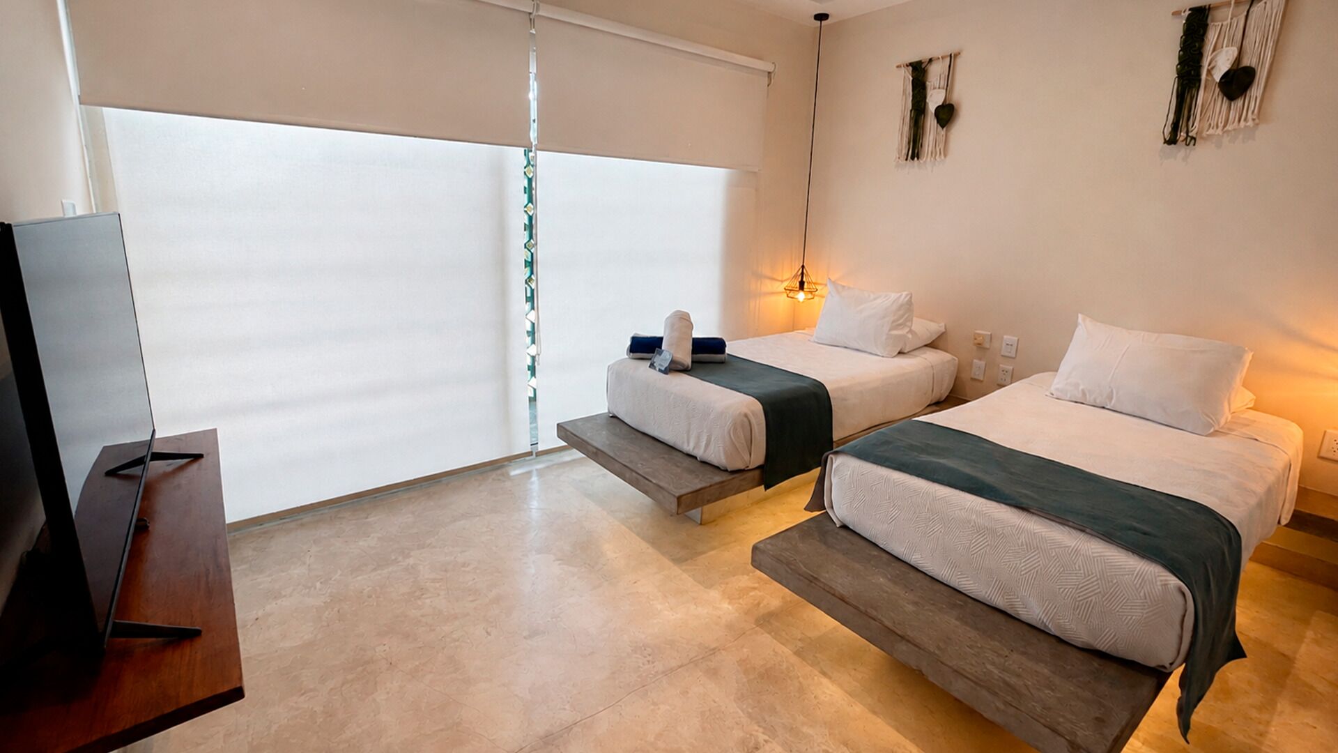 Une chambre d’hôtel avec deux lits, une télévision et une grande fenêtre équipée de stores.