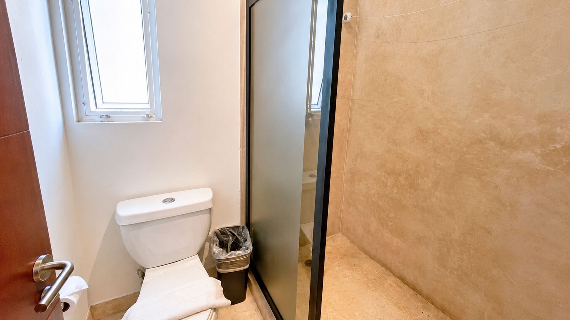A bathroom with a toilet, a trash bin, and a window.