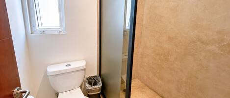 A bathroom with a toilet, a trash bin, and a window.