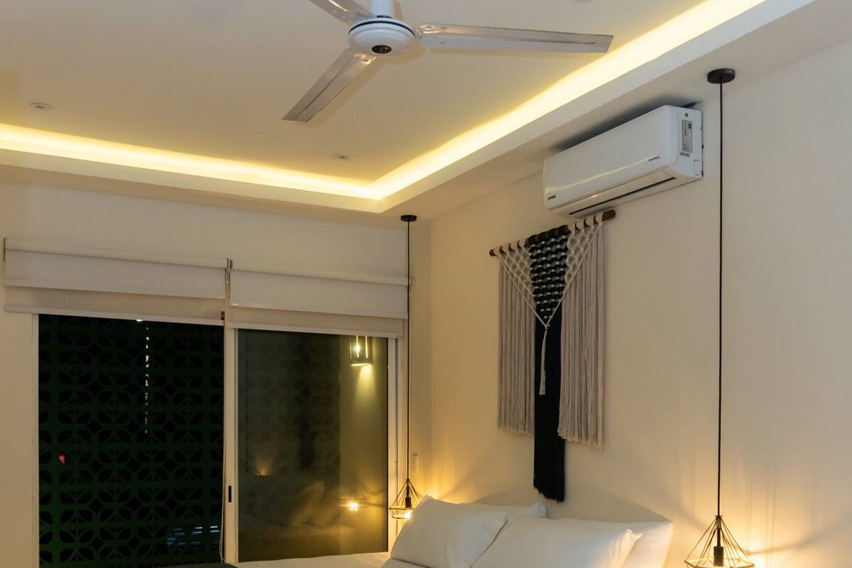 Un dormitorio moderno con cama suspendida, ventilador de techo, equipo de aire acondicionado e iluminación ambiental.