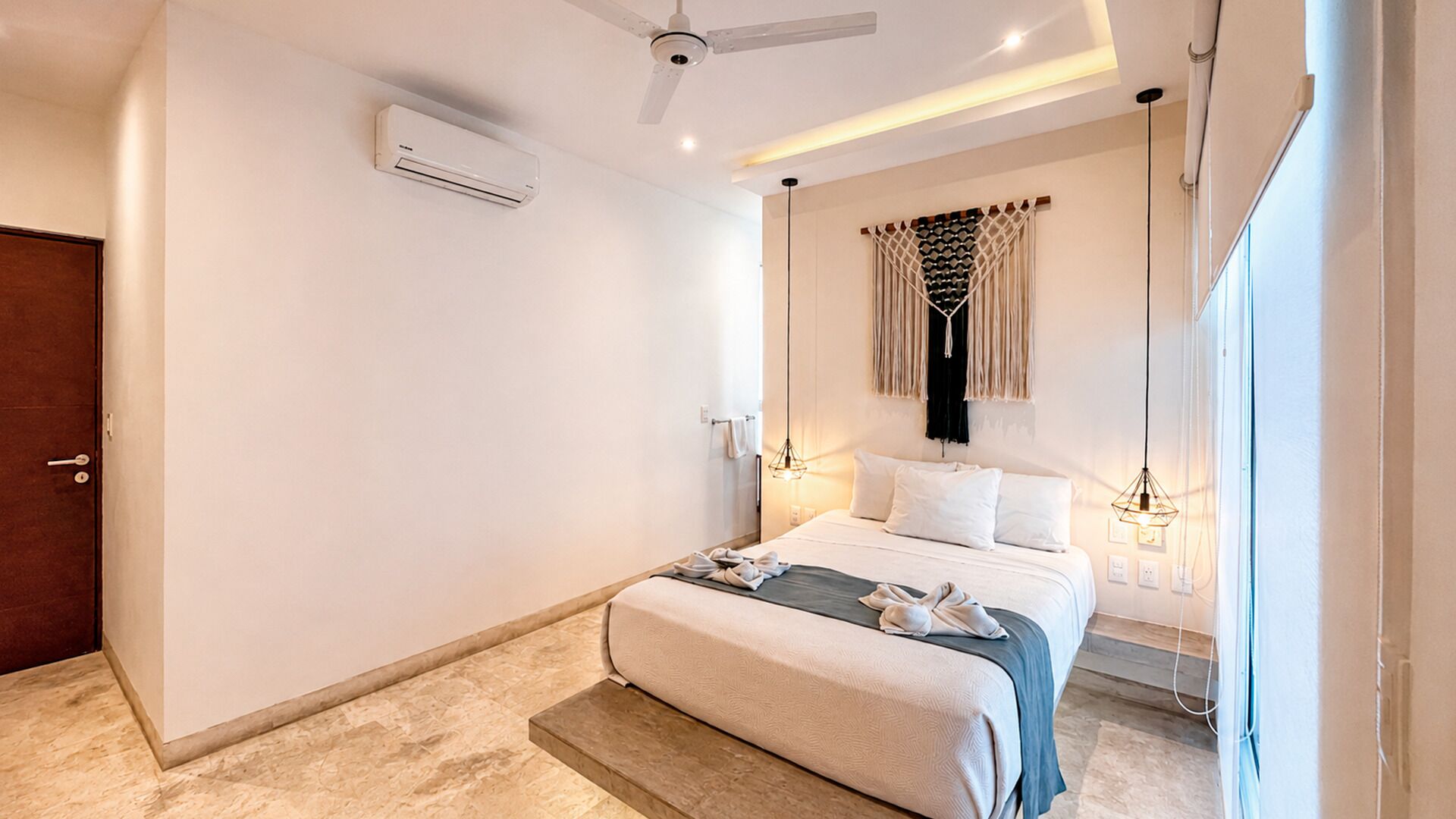 Un dormitorio moderno con cama, lámparas de noche, un equipo de aire acondicionado y un ventilador de techo.