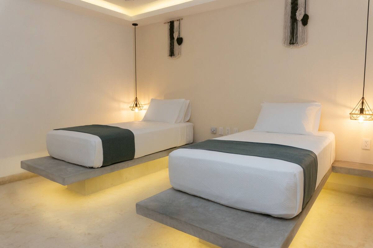 Una habitación de hotel moderna con dos camas, cada una con una lámpara colgante original y un tapiz de macramé en la pared.