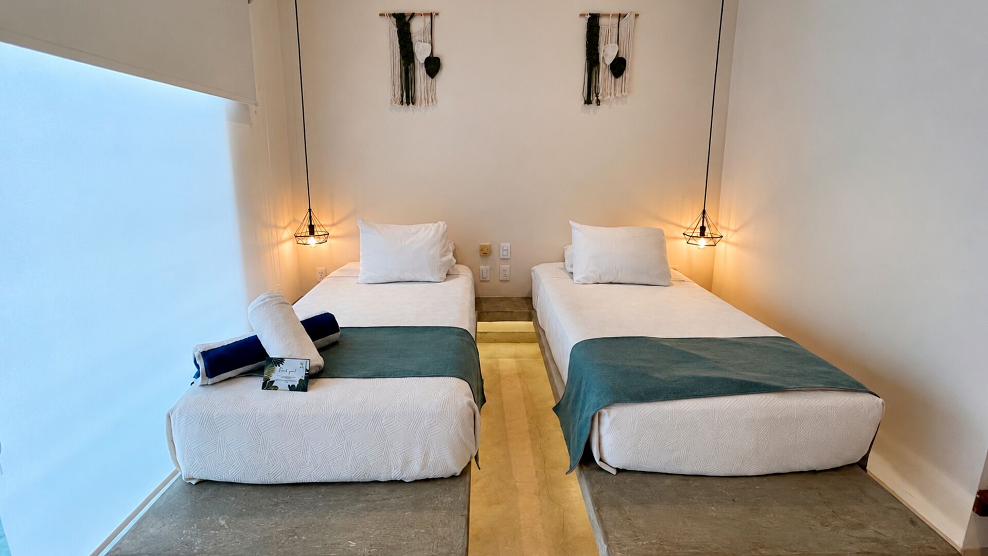 A twin room with two beds, a small table, and a wall-mounted light fixture.
