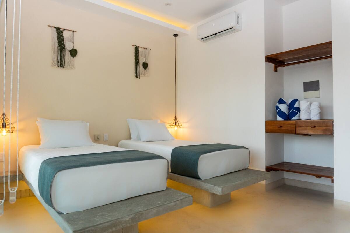 Habitación de hotel con dos camas, un pequeño estante de madera y adornos en la pared.