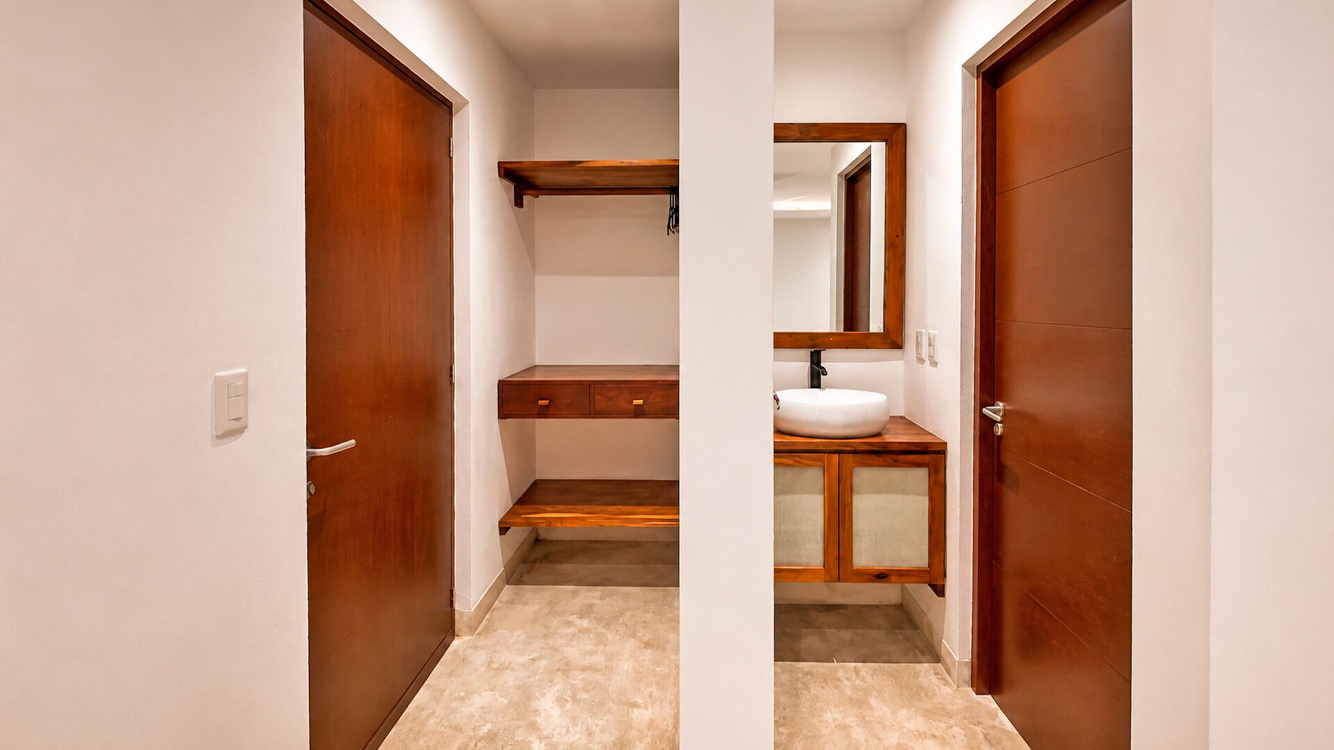 Un corridoio stretto con porte in legno e un bagno con lavandino e specchio.