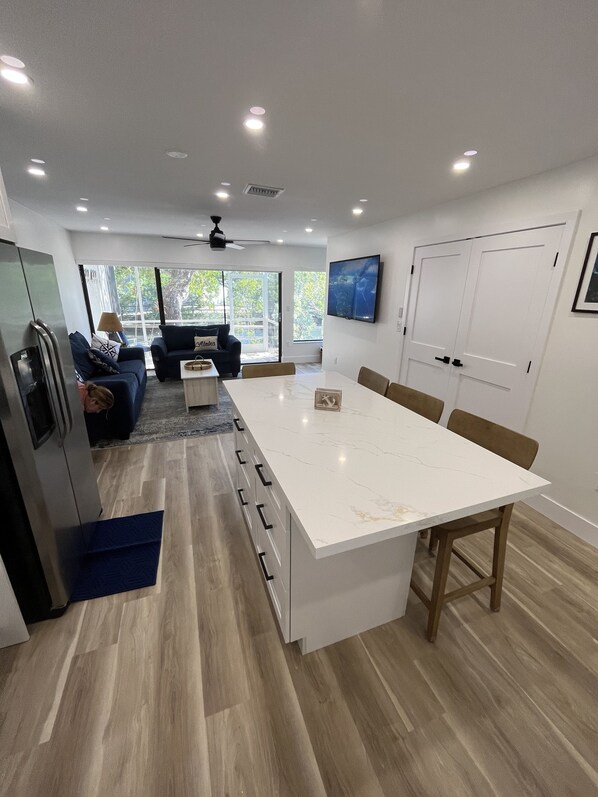 A modern kitchen with a central island, a dining area with a large table, and a living room with a sofa and a TV. - Key Largo Lagoon View Townhome (Key Largo)