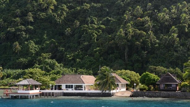 Una propiedad costera con muelle, una edificación principal y una construcción más pequeña, rodeada de exuberante vegetación tropical.