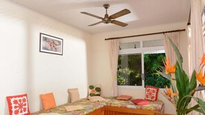 Una habitación acogedora con una cama de madera tipo banco, un ventilador de techo, una ventana con cortinas y un cuadro en la pared.