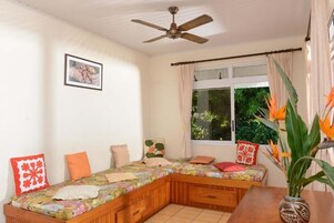 A cozy room with a wooden bench bed, a ceiling fan, a window with curtains, and a framed picture on the wall.