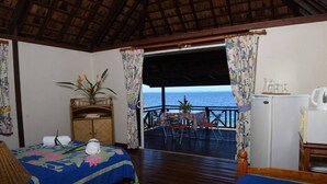 Una habitación con dos camas, una mesa pequeña con sillas, un refrigerador y vista al océano.