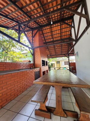 Un porche cubierto al aire libre con pared de ladrillo, una mesa de madera y bancos.