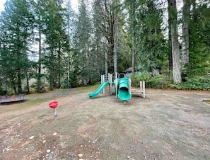 Un terrain de jeux avec un toboggan et une balançoire, entouré d’arbres.