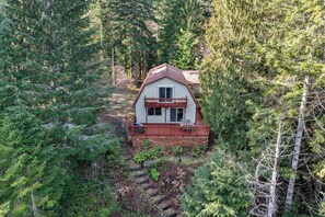 A cabin with a deck, surrounded by dense forest. - Lake Cushman Retreat • Beaver Pond • Kayaks (Hoodsport)