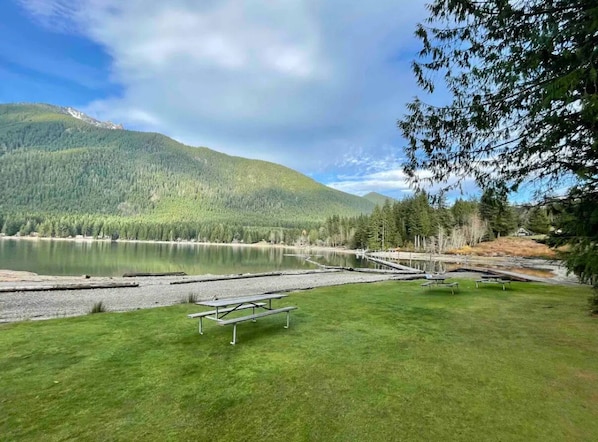 Une vue sur le lac, avec un espace pique-nique, une jetée et une montagne boisée en arrière-plan.