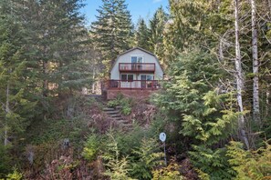 A two-story cabin with a balcony, surrounded by dense forest.