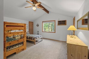 Une chambre avec un lit superposé, un bureau, une lampe, un ventilateur de plafond, une fenêtre donnant sur les arbres et un radiateur fixé au mur.