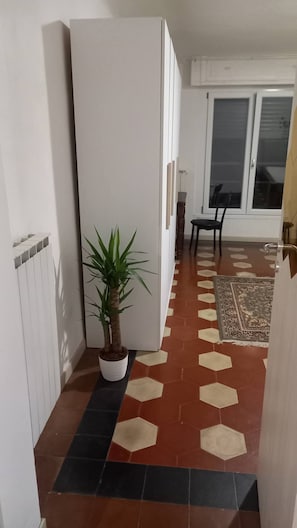 En hall med en krukväxt, en stol, en mönstrad matta och en skjutdörr i glas som leder ut till en balkong.