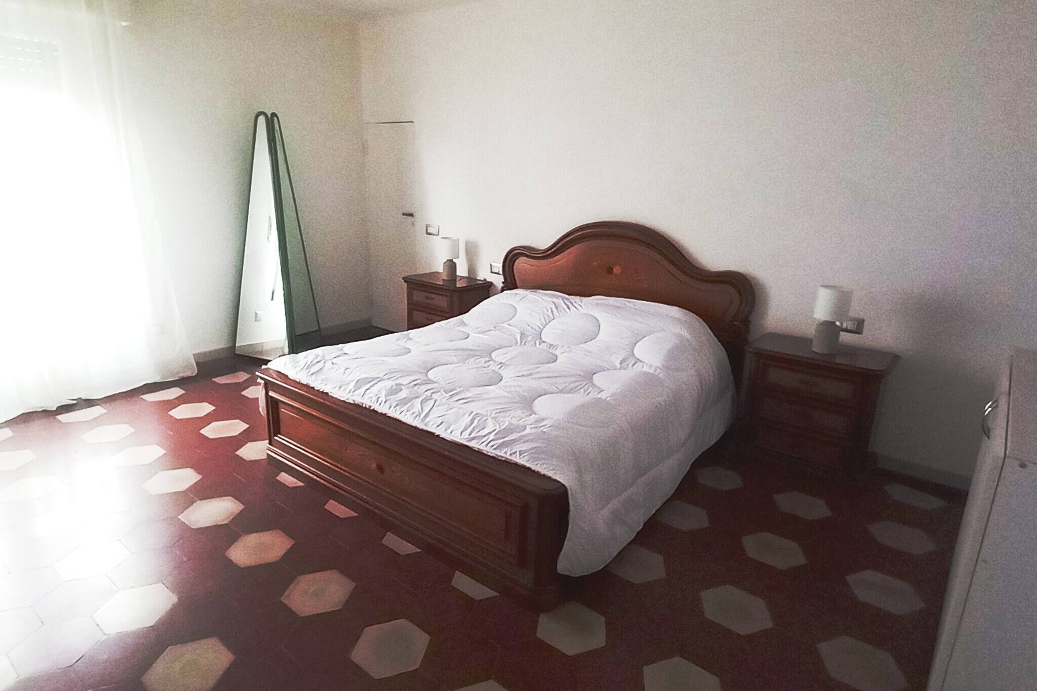 A bedroom with a wooden bed, two bedside tables, a nightstand, and a mirror.
