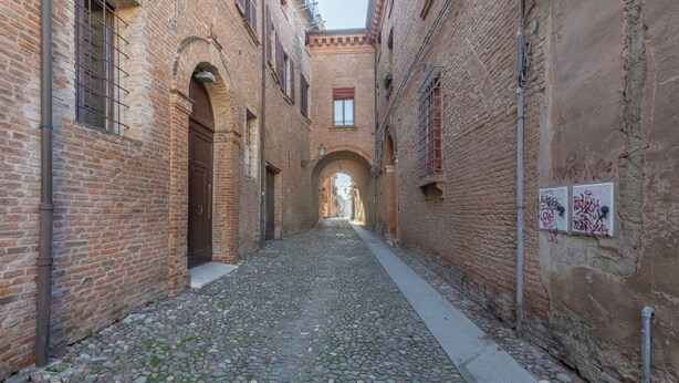 Un estrecho callejón adoquinado con edificios de ladrillo, arcos de entrada y un pasaje central.