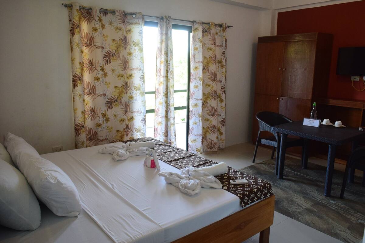 A hotel room with a bed, a desk, a chair, and a wardrobe.