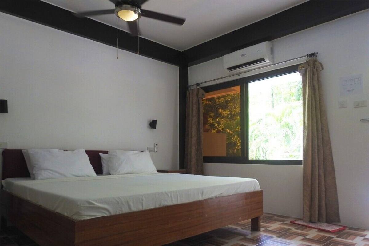 A bedroom with a bed, a ceiling fan, an air conditioning unit, a window with curtains, and a tiled floor.