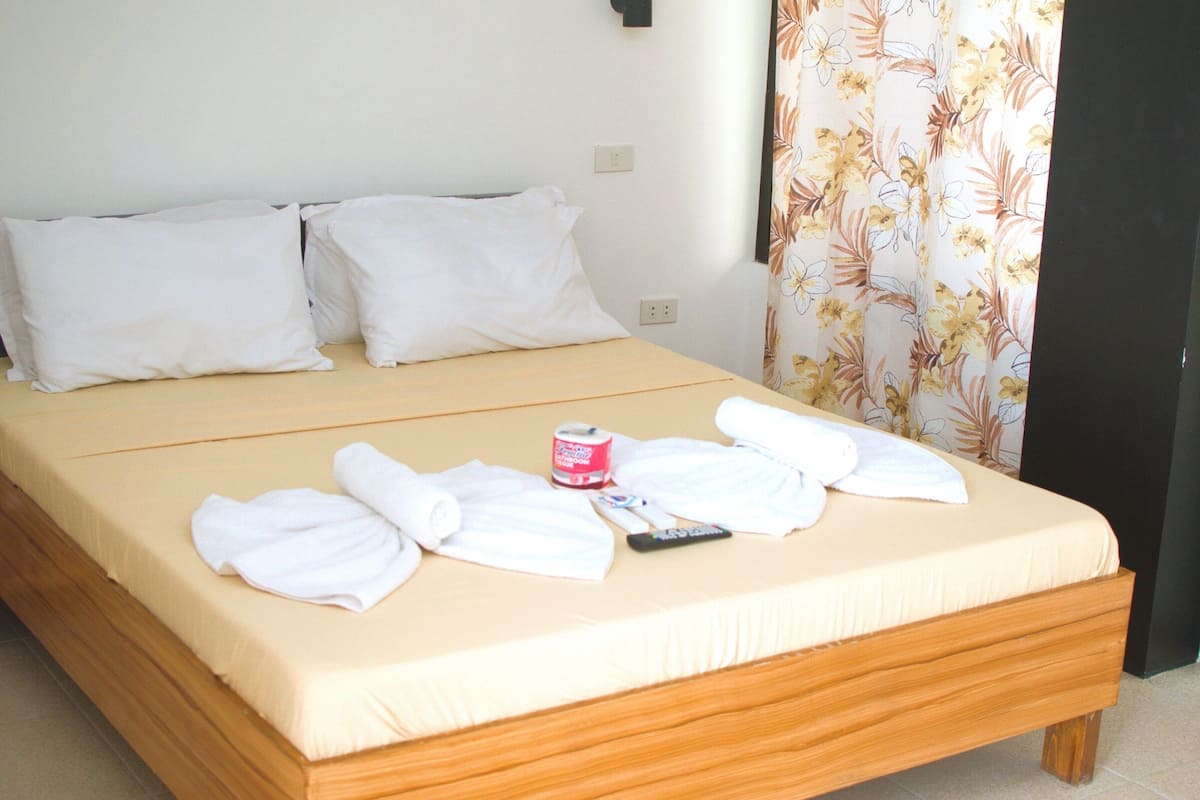 A bed with white linens, a remote control, and a roll of toilet paper.